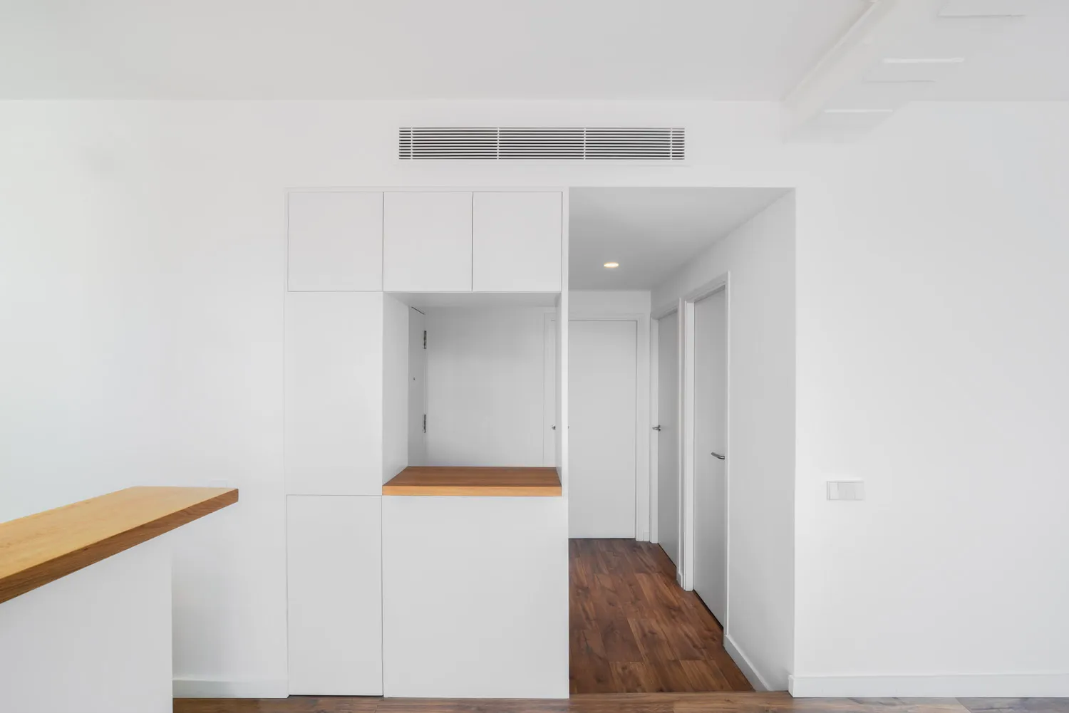 Armari blanc a mida amb una fornícula de fusta i, al costat, el passadís amb parquet cap a les habitacions.